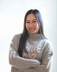 Taupe knit sweater with stitched writing on chest from Favored and Common